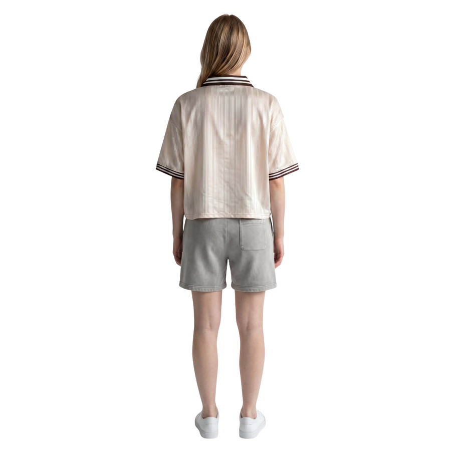 Back view of a woman wearing a NILO beige striped polyester polo tee with relaxed fit and grey shorts
